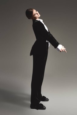 Moda konsepti. Siyah kadife takım elbise ve gri arka planda beyaz gömlek giymiş zarif bir genç kadının tam boy portresi.. 