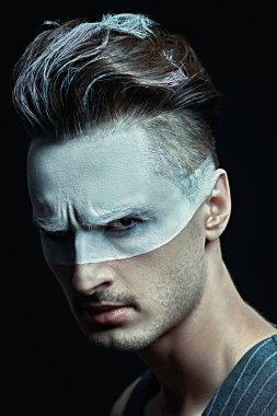 Sanat konsepti. Acımasız, ciddi bir adamın portresi somurtkan, yüzünde beyaz boya ve siyah arka planda saçlar. Erkek güzelliği, moda. Saç stili ve kozmetik.