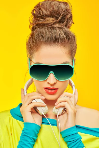 Cool modern girl wearing colorful clothes and sunglasses listens to music in headphones. Studio portrait on a yellow background. Bright lifestyle. Party.