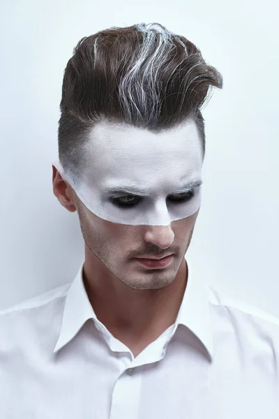 Fashion art portrait of a handsome man with white paint on his face and hair posing in white shirt on a white background. Male beauty, fashion. Hairstyle and cosmetics.