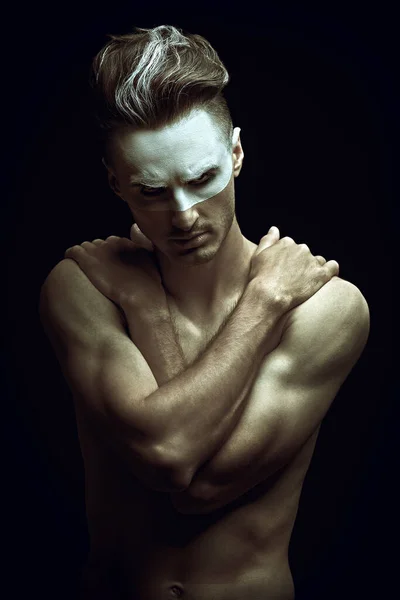 Brutality. Art portrait of an aggressive muscular naked man with white paint on his face posing on a black background.