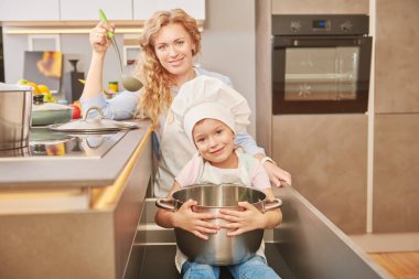 Komik kız ve annesi birlikte yemek pişiriyorlar. Mutlu bir aile. Sağlıklı beslenme.