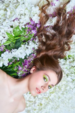 Bahar güzeli. Parlak makyajlı ve çiçekli arka planda gözleri kapalı bir kızın portresi. Makyaj ve makyaj malzemeleri. Boşluğu kopyala.