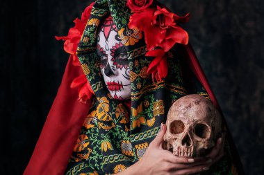 Calavera Catrina 'nın kafatası tutarken çekilmiş yakın plan bir portresi. Şeker kafa makyajı. Dia de los muertos. Ölüler Günü. Cadılar Bayramı.