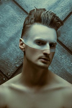 Erkeklerin güzellik anlayışı. Yüzünde beyaz boya olan ve grunge arka planda poz veren yakışıklı çıplak bir adamın portresi..