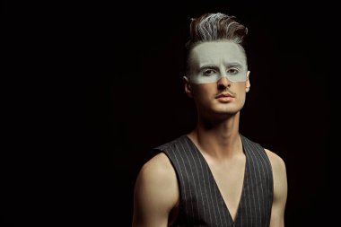 Yüzünde beyaz boya ve fotokopi alanı olan siyah bir arkaplan olan yakışıklı bir gencin sanat portresi. Erkek güzeli, moda. Saç stili ve kozmetik.