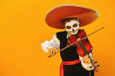 Kafatası şekeri makyajlı yakışıklı çocuk parlak sarı arka planda keman çalıyor. Cadılar Bayramı. Dia de los muertos. Ölüler günü. Boşluğu kopyala.