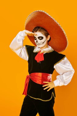 Kafatası şekeri makyajlı yakışıklı bir çocuğun portresi parlak sarı arkaplandaki mesafeye bakıyor. Cadılar Bayramı. Dia de los muertos. Ölüler Günü. 