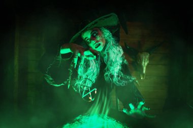 Korkunç yaşlı cadı, sihirli yeşil ışıkla çevrili kazanında büyücülük yapıyor. Cadılar Bayramı. Korkunç hikayeler..