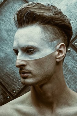 Erkeklerin güzellik anlayışı. Yüzünde beyaz boya olan ve grunge arka planda poz veren yakışıklı çıplak bir adamın portresi..