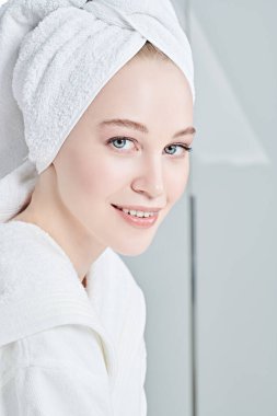 Beyaz bornozlu güzel bir genç kadın portresi ve duş aldıktan sonra saçının etrafına bir havlu. Güzellik, vücut bakımı, kaplıca.