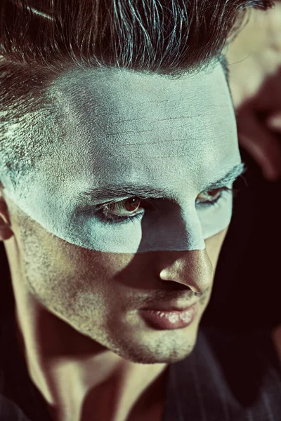 Sanat konsepti. Suratında beyaz boya, arka planında koyu renk saç olan acımasız, ciddi bir adamın portresi. Erkek güzelliği, moda. Saç stili ve kozmetik.