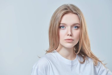 Kameraya gülümseyen sarı saçlı ve doğal makyajlı güzel bir genç kadının portresi. Beyaz bir arka planda stüdyo çekimi. Güzellik endüstrisi. Mutlu yaşam konsepti.