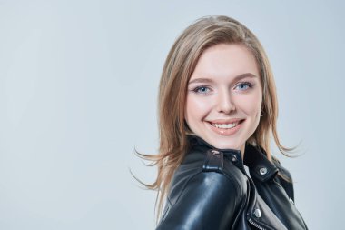 Sarışın, güzel mavi gözlü, beyaz arka planda siyah deri ceketli çekici bir genç kadın. Güzellik, moda. 