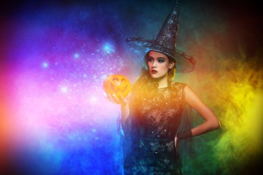 Büyülü arka planda balkabağı tutan cadı kostümlü güzel bir bayan. Cadılar Bayramı. Kutlama.