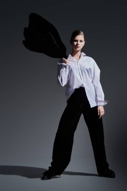 Moda konsepti. Siyah kadife takım elbise ve gri arka planda beyaz gömlekle hareket eden zarif genç bir kadının tam boy portresi.. 