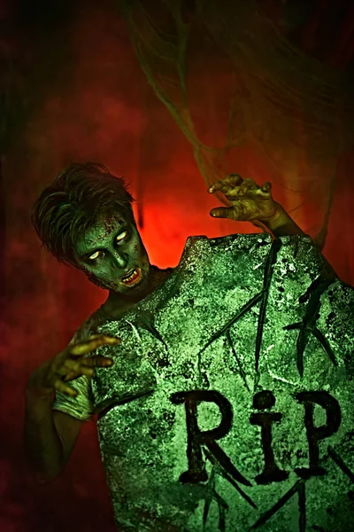 Korkunç Cadılar Bayramı. Korkunç zombi çocuk mezarlıktaki mezar taşının arkasından dikizliyor. Boşluğu kopyala.