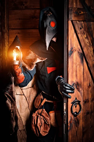 A doctor in a plague suit walks through the door with a lantern in his hand. Ages. Historical reenactment. Halloween.