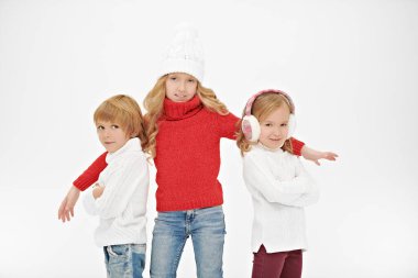Stüdyoda birlikte poz veren kışlık elbiseli üç güzel çocuk. Beyaz arka plan. Kış modası, kış aktiviteleri. Noel ve Yeni Yıl.