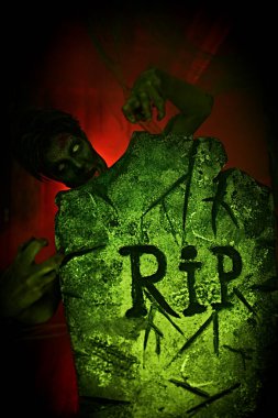 Korkunç Cadılar Bayramı. Korkunç zombi çocuk mezarlıktaki mezar taşının arkasından dikizliyor. Boşluğu kopyala.