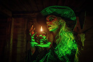 Kafatası şeklinde bir şamdanda mum tutan bir cadı. Cadılar Bayramı. Büyücülük..