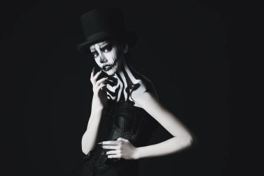 Siyah arka planda kabak kafatası makyajı olan erkek silindir şapkalı zarif genç bir kadın. Balkabağı kraliçesi. Cadılar Bayramı için kostüm ve makyaj. Boşluğu kopyala.