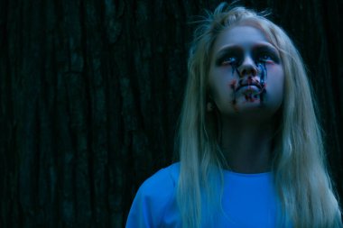 Ormandaki bir korku filminden yukarı bakan korkutucu, soluk benizli bir kızın portresi. Zombi, Cadılar Bayramı.