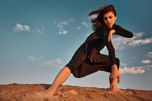 Moda fotoğrafı. Çölde poz veren uzun siyah elbiseli güzel esmer kadın. Gökyüzü arkaplanı.