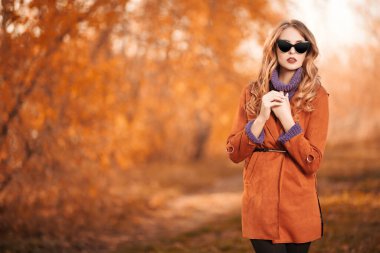 Güzel genç bir kadın sonbahar parkında yürüyor ve gülümsüyor. Sonbahar güzelliği, moda.