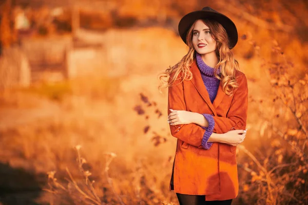 Güzel genç bir kadın sonbahar parkında yürüyor ve gülümsüyor. Sonbahar güzelliği, moda.