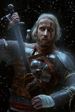 Portrait of a brave medieval warrior in armor with a sword on a snowy background. The Witcher man. clipart