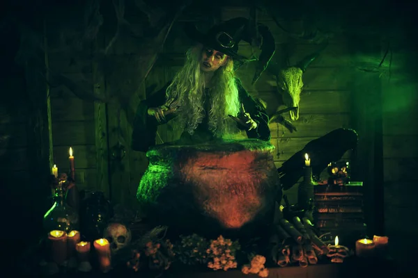 Horrible old witch brews magic potion in her cauldron surrounded by magical green light. Halloween. Scary tales.