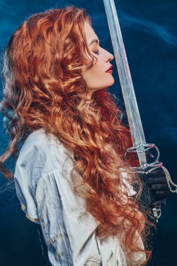 Güzel ve cesur kızıl saçlı bir kadının profil portresi ve savaş çadırı (rapier). 16.-17. yüzyılların tarihi yeniden yapılandırması.