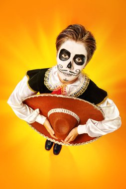 Kafatası makyajlı yakışıklı bir çocuğun portresi parlak sarı arka planda elinde sombrero tutuyordu. Cadılar Bayramı. Dia de los muertos. Ölüler günü. Boşluğu kopyala.
