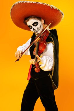 Kafatası şekeri makyajlı yakışıklı çocuk parlak sarı arka planda keman çalıyor. Cadılar Bayramı. Dia de los muertos. Ölüler günü. Boşluğu kopyala.