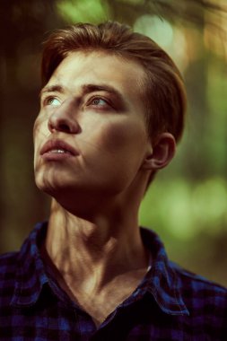 Ormanın gölgesinde duran yakışıklı genç adam ve güneş ışınları yüzüne vuruyor. Erkek güzeli.. 