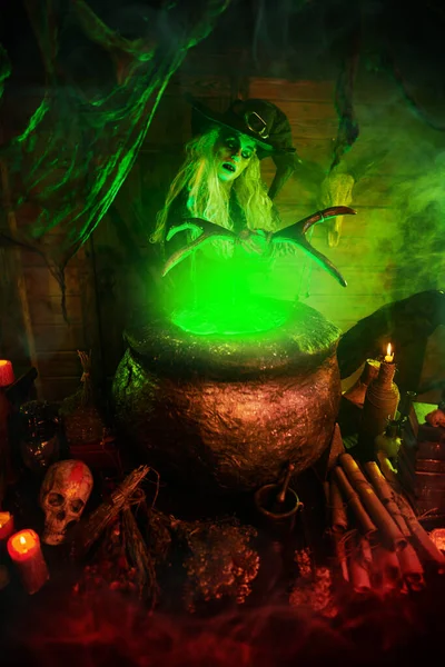 Horrible old witch holding staff above the boiling potion in a cauldron surrounded by a magical green light. Halloween. Witchcraft.