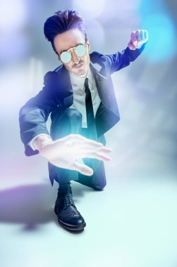 Zarif siyah takım elbiseli, beyaz gömlekli ve güneş gözlüklü, gri arka planda gölgeli bir şekilde poz veren modern tarz bir adam. Modern bir iş adamının tam boy portresi. Erkek modası.