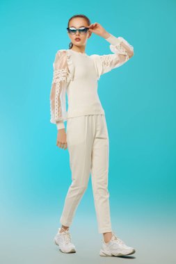 Zarif yaz kıyafetleri ve açık mavi arka planda güneş gözlükleriyle poz veren güzel bir kız. Mutlu gülümseyen kız. Yaz modası. Optikler. 