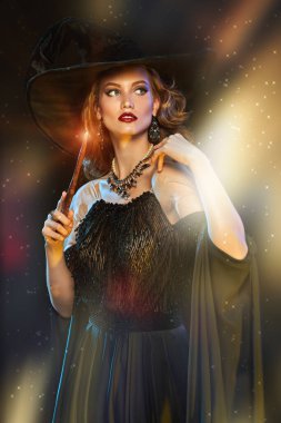 Şapkalı güzel genç bir cadının portresi ve sihirli ışıklarla çevrili sihirli bir değnekle. Cadılar Bayramı kutlaması, parti. 