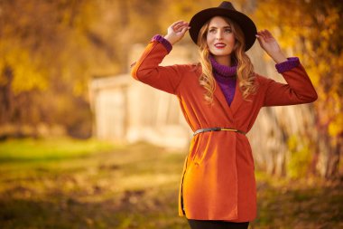 Güzel genç bir kadın sonbahar parkında yürüyor ve gülümsüyor. Sonbahar güzelliği, moda.