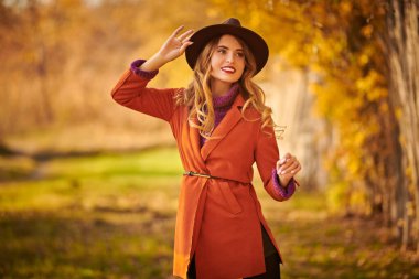 Güzel genç bir kadın sonbahar parkında yürüyor ve gülümsüyor. Sonbahar güzelliği, moda.