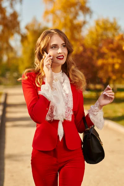 Elegant young woman walks through the beautiful autumn park and talking on the phone. Beauty, fashion. Full length portrait.