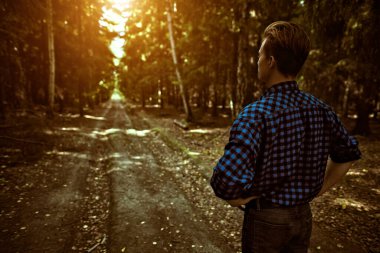 Genç bir adam vahşi bir ormanda arkası dönük duruyor. Uzağa uzanan bir yolda. Macera, özgürlük ruhu. Etkin yaşam biçimi. 