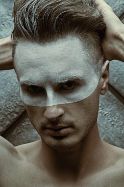 Erkeklerin güzellik anlayışı. Yüzünde beyaz boya olan ve grunge arka planda poz veren yakışıklı çıplak bir adamın portresi..