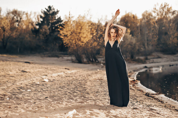 A beautiful young girl is posing in a black dress on beach. Fashion concept.