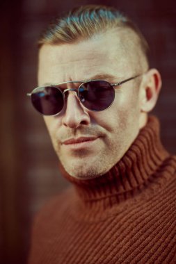 Duvarın arkasında güneş gözlüklü yakışıklı bir adamın portresini yakından çek. Optik tarzı. Erkek güzelliği, moda.