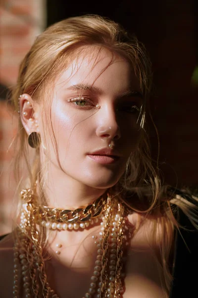 Beauty, fashion and makeup concept. Portrait of a beautiful blonde girl with fresh shiny makeup and gold and pearl jewelry.