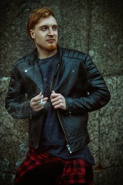 Genç hippi, taş bir duvara karşı sigarayla poz veriyor. Büyük bir şehirde gece hayatı.