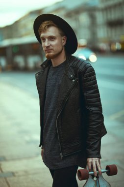 Modern genç hippi adam elinde bir tahtasıyla büyük bir şehrin caddesinde yürüyor. Etkin yaşam biçimi.